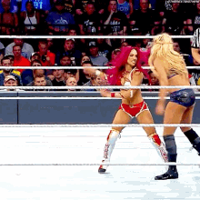 two women are wrestling in a ring with a referee in the background .