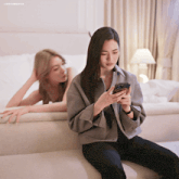 two women are sitting on a couch and one is looking at her phone with a caption that says lingormgifss