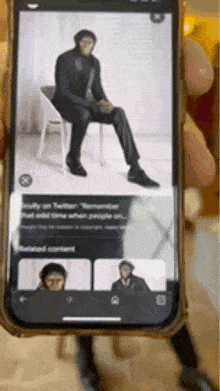 a person is holding a cell phone with a picture of a man sitting in a chair on the screen