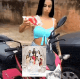 a woman in a blue top is standing next to a pink motorcycle with a poster of a group of women on it