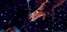 a man and woman are holding hands in the snow while it is snowing .