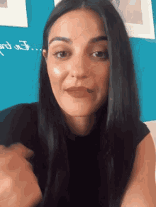 a woman in a black shirt is smiling in front of a blue wall that says i on it