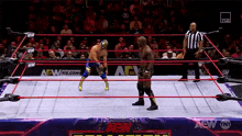 two men are wrestling in a wrestling ring while a referee looks on .