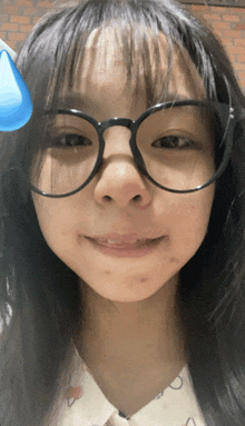 a girl wearing glasses looks at the camera with a blue drop on her forehead