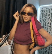 a woman wearing sunglasses and a crop top is holding a pink purse .