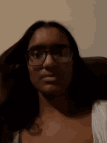 a woman wearing glasses and a white shirt is making a funny face