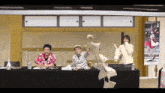 a group of people are sitting at a table with papers flying around them