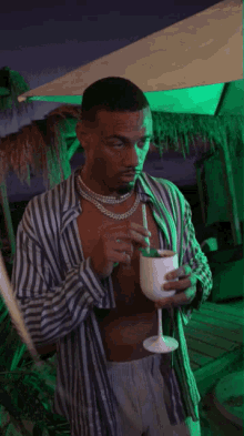 a man in a striped shirt drinks from a glass with a straw