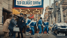 a group of people are walking in front of a sign that says ted gilbert show