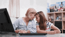 a mother and daughter sit at a desk with a computer
