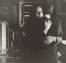 a black and white photo of a woman hugging a man in front of a fireplace with the letter e on it