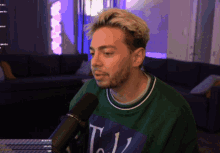 a man wearing a green shirt with the letter t on it stands in front of a microphone