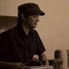 a man wearing a hat is sitting in a chair holding a book and a pen .