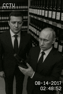 two men in suits and ties are looking at a bottle of wine in front of shelves of wine