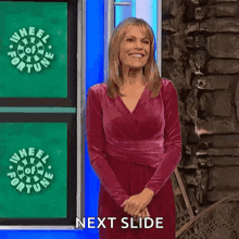 a woman in a red dress is smiling while standing in front of a wheel of fortune logo .