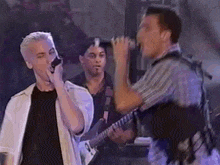 a man is singing into a microphone while another man plays a guitar in the background .