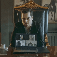 a man in a suit sits in front of a laptop that says minimalmoons on the keyboard
