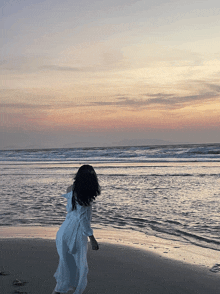 a woman in a white dress is standing on the beach at sunset