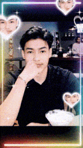 a man in a black shirt is sitting at a table with his hand on his chin surrounded by heart shaped lights .