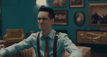 a man in a blue shirt and brown suspenders is sitting on a couch