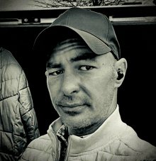 a man wearing a hat and ear buds looks at the camera in a black and white photo