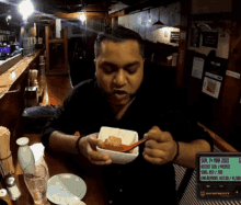 a man sitting at a table eating a bowl of food with a sign behind him that says the last