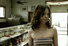 a woman in a striped top is standing in front of a shelf with a can of spaghettios