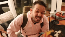 a man with a beard wearing a pink hoodie is sitting in a chair