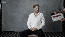 a man in a white shirt sits in front of a bbc logo