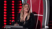 a woman is sitting in a chair with a laptop in front of her and the words #thevoice are visible