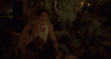 a man is playing a guitar in a dark room while another man looks on .