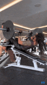 a woman is lifting a barbell in a gym with a tiktok icon in the corner