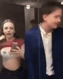 a man in a suit stands next to a woman in a crop top who is holding a cell phone