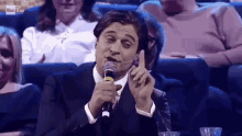 a man in a suit is singing into a microphone while sitting in a theatre .