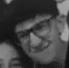 a black and white photo of a young man wearing glasses and smiling .