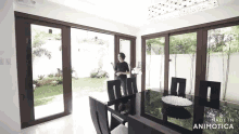 a woman is standing in a dining room with a table and chairs in front of a sliding glass door .