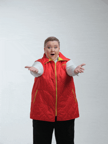 a woman wearing a red vest with a yellow zipper has her arms outstretched and a surprised look on her face