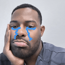 a man with blue tears on his face holds his hand to his face