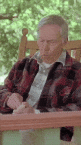 a man in a plaid shirt sits in a rocking chair on a porch