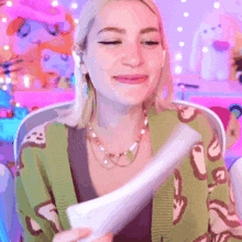 a woman in a green cardigan is holding a piece of paper and smiling