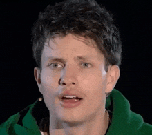 a close up of a man wearing a green hoodie making a funny face .