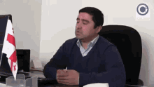 a man sits at a desk in front of a computer with a flag that says georgia on it