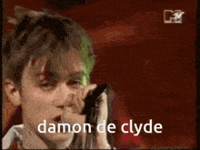 a man with green hair singing into a microphone with the words damon de clyde above him