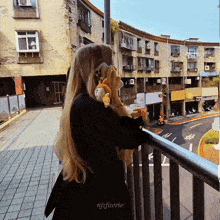 a woman is standing on a balcony holding a stuffed animal and the name njfuerie is on the bottom