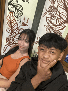 a boy and a girl are posing for a picture in front of a wall with leaves and coffee beans painted on it