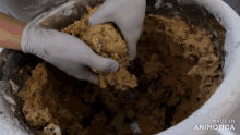 a person is mixing a cookie dough in a metal bowl with the words made in animatica on the bottom