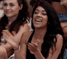a woman in a black tank top is clapping her hands and smiling
