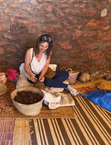 a woman is sitting on a rug in front of a stone wall