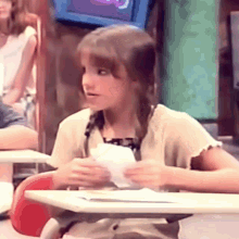 a young girl is sitting at a desk in a classroom with a piece of paper in her hand .