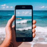 a hand is holding a cell phone with a picture of the ocean on it